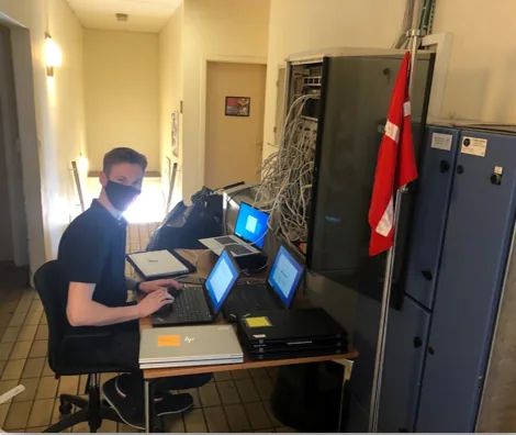Ung mand ved computer til netværksopsætning med dansk flag og servere i baggrunden